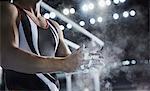 Male gymnast rubbing chalk powder on hands below parallel bars