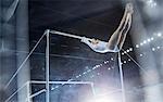 Female gymnast performing on uneven bars in arena