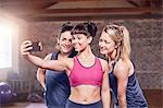 Fit young women in sports clothing taking selfie with camera phone in gym studio