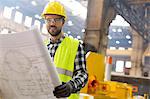 Portrait smiling engineer with blueprints ins steel factory