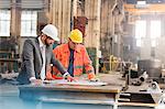 Manager and steel worker engineer reviewing blueprints in factory