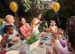 Multi-ethnic multi-generation family clapping celebrating birthday with fireworks cake at patio table