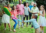Multi-ethnic multi-generation family cheering boy hitting pinata at birthday party