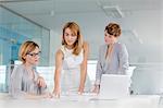 Female architects discussing blueprint at laptop in conference room meeting