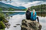 Couple sitting on rock looking at tranquil lake, Loch an Eilein, Scotland