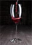 Pouring red wine from bottle to the glass on wooden board