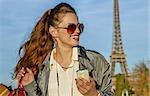 Get your bags ready for the Paris autumn sales. Portrait of happy young elegant woman in sunglasses with shopping bags looking aside while holding smartphone near Eiffel tower