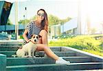 Happy Hipster Girl with her Dog in the City Park. Smiling Woman with Pet Outdoors at Sunset. Trendy Fashion Female. Toned and Filtered Photo. Modern Youth Lifestyle Concept.