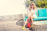 Young Fashion Woman Outdoors. Trendy Street Style Girl in Summer Clothing and Sunglasses Sitting. Toned Photo with Copy Space.