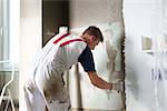 Thirty years old manual worker with wall plastering tools renovating house. Plasterer renovating indoor walls and ceilings with float and plaster.