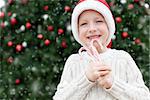 little boy in santa's hat holding candy canes enjoying snowy christmas time