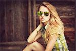 Portrait of a Sensual Fashion Hipster Girl on Wooden Background. Beautiful Blonde Woman in Sunglasses Outdoors. Street Style Female. Vintage Toned Photo with Copy Space.