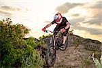 Professional Cyclist Riding the Bike Down Rocky Hill at Sunset. Extreme Sport Concept.