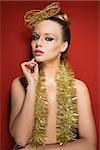 sensual female with sparkly golden make-up, glitter hair-style accessory and tinsels on nude breast. Red background, luxury creative style