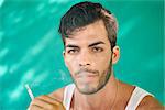 Real Cuban people and emotions, portrait of young hispanic man from Havana, Cuba looking at camera with serious expression, smoking cigarette and blowing smoke