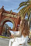 in Barcelona for a perfect winter. Seen from behind young woman in earmuffs near Arc de Triomf in Barcelona, Spain looking at the map