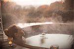 Serene woman soaking in steaming hot tub with autumn tree view