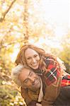 Portrait playful couple piggybacking in autumn woods