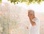 Man talking on cell phone and drinking coffee on autumn patio