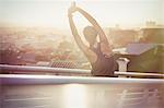 Female runner stretching arms on urban footbridge at sunrise