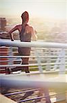 Female runner running on sunny urban footbridge at sunrise