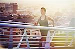 Determined female runner running up urban footbridge at sunrise