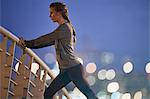 Determined female runner stretching legs on footbridge at dawn