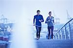 Runner couple running on urban footbridge at dawn