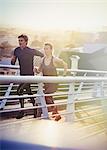 Runner couple running on sunny urban footbridge at sunrise