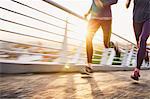 Runner couple running on sunny urban footbridge at sunrise