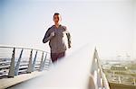 Female runner running on sunny urban footbridge