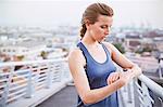 Female runner checking smart watch fitness tracker on urban footbridge