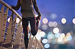 Female runner stretching leg on footbridge at dusk