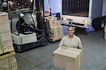 Portrait smiling worker carrying cardboard box at distribution warehouse loading dock