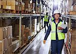 Portrait smiling female worker holding clipboard in aisle of distribution warehouse