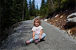 Little girl sitting on gravel road in forest, Vancouver, British Columbia, Canada