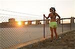 Female athlete daydreaming by wire fence at sunset, Van Nuys, California, USA