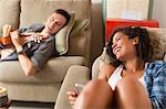 Young couple relaxing on sofa using digital tablet and playing guitar