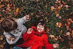 Overhead portrait of girl and toddler sister lying on grass and autumn leaves