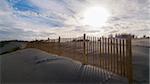 Sand dunes and wooden fence with bright sun shining through clouds along the Atlantic Ocean in Royan, France