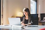 Young businesswoman at office desk typing on laptop