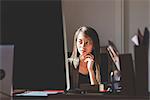 Young businesswoman at office desk gazing at computer