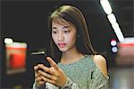 Young woman reading smartphone on railway platform at night