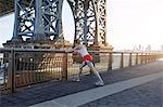 Young woman exercising outdoors, stretching underneath Williamsburg Bridge, New York City, USA