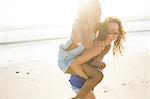 Young woman piggybacking female friend on beach, Cape Town, South Africa