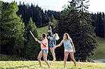 Three female adult friends blowing and jumping for bubbles in field, Sattelbergalm, Tirol, Austria