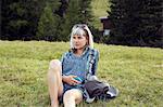 Woman sitting in field holding smartphone, Sattelbergalm, Tirol, Austria