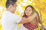 Young man wrapping tartan scarf around girlfriend in autumn park, Beijing, China