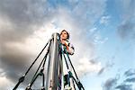 Boy in astronaut costume gazing at top of climbing frame against dramatic sky