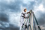 Boy in astronaut costume gazing from top of climbing frame against dramatic sky